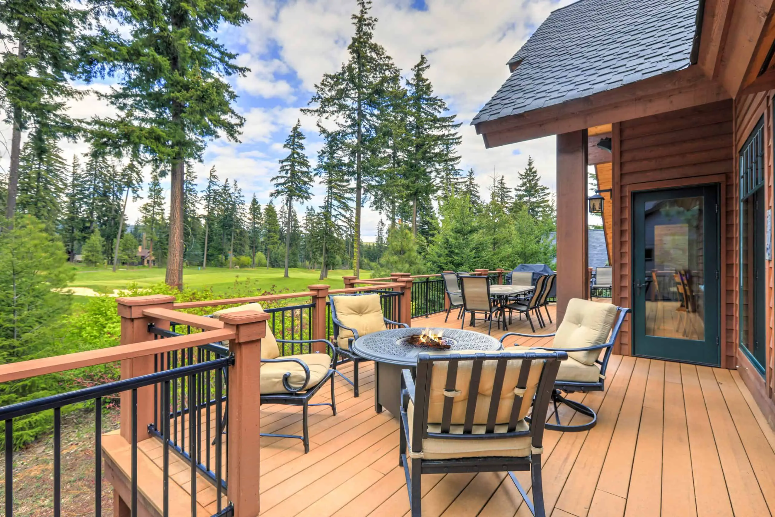 Beautiful large cabin home with large wooden deck and chairs with table overlooking golf course.